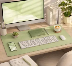 Light green desk pad on a modern home office desk with keyboard, mouse, notebook, coffee cup, and computer in a clean minimalist workspace.