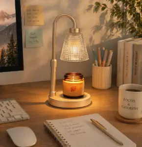 Gold candle warmer lamp on a home office desk with a scented candle, notebook, coffee mug, keyboard, pens, and warm cozy lighting.