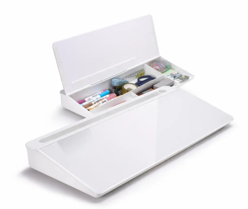 Minimalist white desk organizer with built-in storage compartments and angled writing surface, shown open with pens, tape, and office supplies neatly arranged.